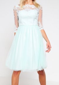 Robe vert menthe clair avec un corps ajusté, des manches en dentelle transparente et une jupe en tulle évasée. Broderie florale complexe au niveau du col.