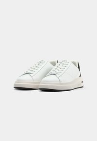 Sneakers bianchi in pelle con una finitura liscia, dotati di una suola spessa beige, dettaglio del tallone nero e chiusura con lacci. Logo sulla linguetta e sul lato.