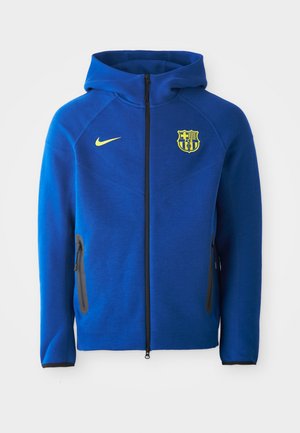 Blaue Kapuzenjacke aus weichem Stoff, mit einem Reißverschluss vorne, schwarzen Akzenten und einem gelben Nike-Logo sowie einem Vereinswappen auf der Brust.