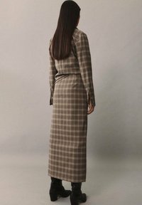 Robe longue marron à carreaux, silhouette ajustée, manches longues et longueur mi-mollet, associée à des bottes noires montant jusqu'aux genoux.