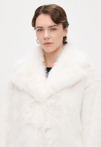 Cappotto in finta pelliccia bianca con ampio collo morbido e finitura testurizzata. Il design presenta una vestibilità rilassata e bottoni sulla parte anteriore.