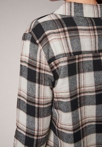 Camicia in flanella a quadri bianca e nera con accenti marroni, colletto classico e vestibilità rilassata, che mette in evidenza una texture morbida.