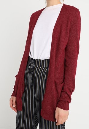 Cardigan bordeaux en tissu doux, avec une ouverture à l'avant, des manches longues et des poches. Associé à un pantalon à rayures noir et blanc.