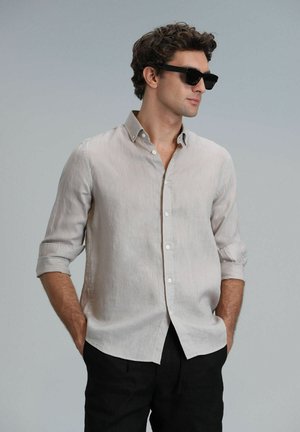 Light beige linen shirt with rolled sleeves, button-down collar, and white buttons. Paired with black pants; sunglasses complete the look.