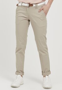 Beige Chinos mit schmaler Passform und aufgerollten Säumen, mit vorderen Taschen und einem weißen geflochtenen Gürtel. Kombiniert mit weißen Sneakers.