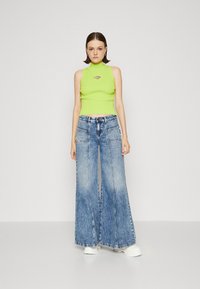 Lime green cropped ribbed tank top with a silver accent, paired with oversized blue denim jeans featuring front pockets and frayed hems.