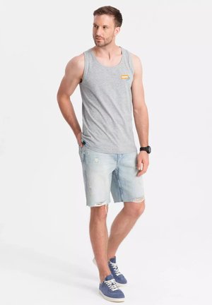 Graues Baumwoll-Top mit einem orangefarbenen Logo, kombiniert mit hellblauen Jeansshorts mit ausgefransten Kanten und distressed Details. Blaue Turnschuhe.