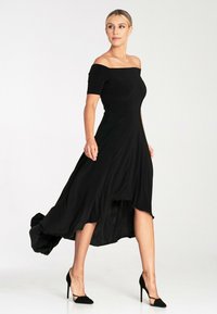 Czarna sukienka bez ramiączek z krótkimi rękawami, płynącą linią dołu i dopasowanym górą, wykonana z lekkiego materiału. Noszona z czarnymi szpilkami.