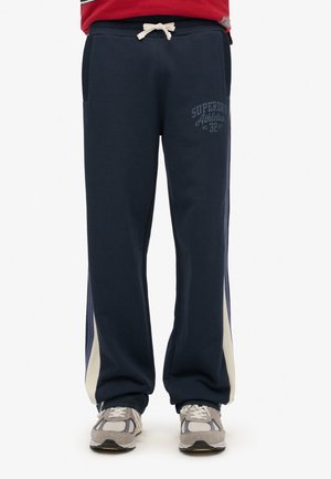 Marineblauwe trainingsbroek met een tailleband met trekkoorden, zijzakken en contrasterende lichtgrijze zijpanelen. Bevat subtiele logo-tekst op de voorkant.