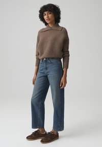 Brown ribbed knit sweater with a collar, paired with high-waisted blue straight-leg jeans and brown suede sneakers. Plain background.