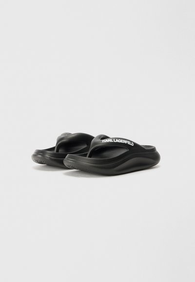 Des tongs noires avec une semelle texturée, dotées d'une large sangle et d'un détail de logo en blanc. Fabriquées en matériau en caoutchouc léger.
