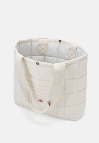 Torebka tote w kolorze kremowym, o wyraźnym kształcie, z długimi materiałowymi uchwytami oraz gładkim, wyprofilowanym wnętrzem z widocznymi szwami.