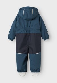 Mono infantil impermeable de invierno en azul y negro con capucha, puños elásticos, cintas reflectantes y correas para los pies, visto desde la parte posterior.