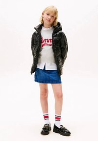 Sort dunjakke, grå sweater med rød logo, hvid skjorte, blå denimnederdel og sorte sko med gyldne detaljer, kombineret med strømper med striber.