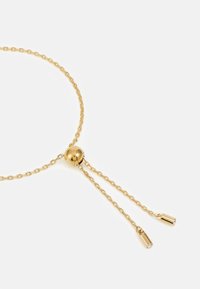 Collar de tono dorado con un colgante redondo liso y dos cadenas ajustables que terminan en acentos cilíndricos, con pequeñas piedras preciosas transparentes.