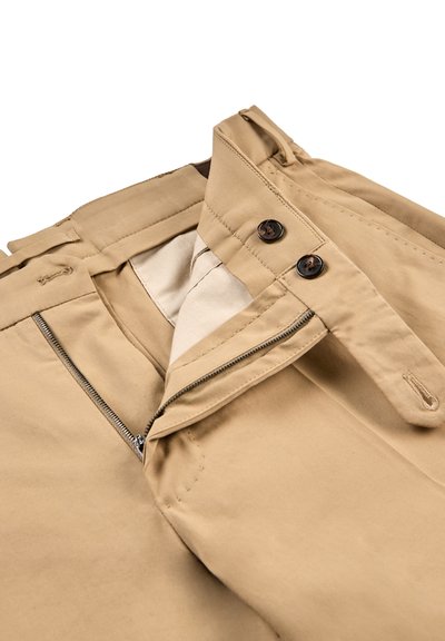 Pantalon beige avec fermeture éclair ouverte, deux boutons foncés sur la ceinture, et passants de ceinture, présenté à plat sur fond blanc.