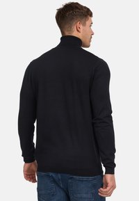 Schwarzer, langärmeliger Rollkragenpullover aus strukturiertem Strickstoff. Verfügt über ein figurbetontes Design und glatte Nähte. Ansicht von hinten.