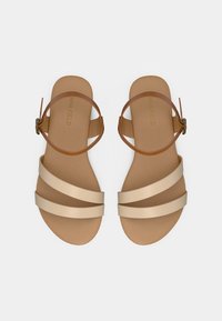 Πλατιά σανδάλια με ταμπά λουράκι στον αστράγαλο και μπεζ χιαστί λουριά. Απαλή ματ υφή, μίνιμαλ σχεδιασμός και λεία σόλα.
