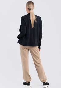 Sweatshirt navy avec une coupe décontractée, associé à un jogging beige avec des poignets élastiques et des coutures latérales. Des baskets noires complètent le look.