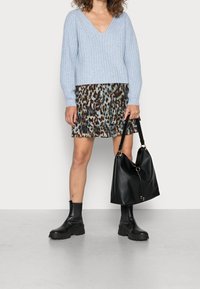 Jasnoniebieski prążkowany sweter z dzianiny z dekoltem w serek, noszony na plisowanej spódnicy w zwierzęcy wzór w odcieniach beżu, brązu i zieleni. Czarna torba na ramię i botki za kostkę.