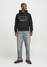 Sudadera de algodón negra con un gráfico en la parte delantera y cordón ajustable, combinada con jeans de mezclilla azul claro y botas marrones.