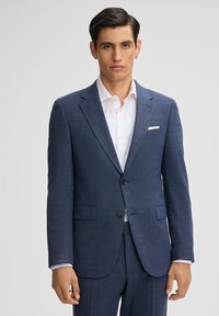 Giacca blu scuro in tessuto testurizzato, con rever a punta, chiusura con un bottone e due tasche frontali. Camicia bianca sotto.