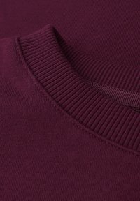 Jersey burdeos con un cuello redondo acanalado y una textura suave. La tela presenta un color sólido sin patrones ni adornos.