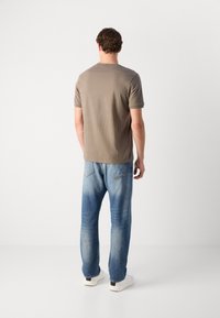 Un tricou gri cu mânecă scurtă, purtat împreună cu blugi drepti de culoare albastru deschis și adidași albi. Țesătura pare moale și cu o textură netedă.