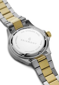 Stålklokke med gullakenter, sølvfarget rustfritt stålarmbånd, solid bakdeksel med påskriften "316L RUSTFRITT STÅL" og "VANNTETT".