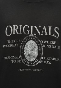 Κείμενο «ORIGINALS» πάνω από οβάλ τοπίο βουνών με ετικέτα «Βουνά Adirondack Νέα Υόρκη» με φράσεις για δημιουργικότητα και άνεση σε μαύρο ύφασμα.