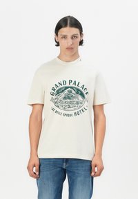 Kremfarget bomull T-skjorte med et grønt grafikk av et fjell og teksten "GRAND PALACE LA BELLE EPOQUE HOTEL" i et sirkulært design.