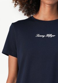 Navy modrá tričko s krátkým rukávem vyrobené z měkké látky, s bílou výšivkou loga "Tommy Hilfiger" na hrudi.