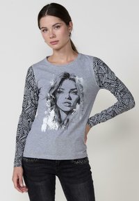 Camiseta de manga larga gris con un gráfico impreso en la parte frontal y mangas negras con estampado. Presenta un cuello redondo y un ligero estiramiento en la tela.