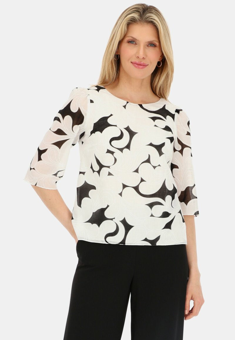 Biała bluzka z czarnym florystycznym wzorem, półprzezroczystymi rękawami, okrągłym dekoltem oraz luźnym krojem, w połączeniu z czarnymi spodniami.