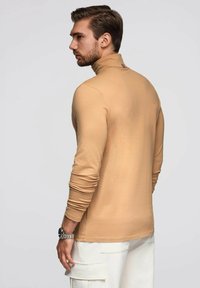 Beige Langarm-Turtleneck-Shirt aus weichem Material, mit einer taillierten Passform und subtilen Farbvariationen. Minimalistisches Styling.