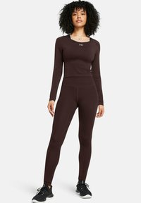 Brown long-sleeve athletic top and matching tight leggings, fitted design, smooth texture, with black footwear featuring a textured sole.