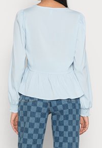 Light blue peplum blouse with long sleeves and ruched shoulders, paired with checked denim pants featuring varying shades of blue.