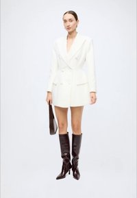 White double-breasted blazer mini dress with a tailored fit, paired with knee-high black heeled boots and a black handbag. Smooth texture.