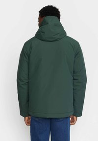 Green waterproof jacket with a hood, featuring a smooth texture and a straight cut. Visible stitching and a relaxed fit in the back.