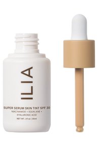 ILIA Super Serum Skin Tint SPF 30 i en vit flaska med brunt text, tillsammans med en brun pipett med en vit glödlampa. 30ml.