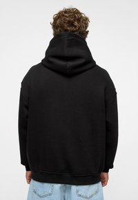 Zwarte hoodie met een losse pasvorm, vervaardigd van een stijlvolle stof met een textuur en geribbelde boorden en zoom. Eenvoudig ontwerp, zonder zichtbare patronen of logo's.