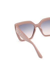 Gafas de sol de plástico marrón con lentes degradados, forma angular de ojo de gato, acentos decorativos de logo y patillas gruesas.
