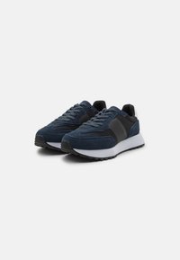 Sneakers blu navy con tomaia in suede, dettagli neri e suola intermedia bianca. Suola in gomma testurizzata per una presa migliore, caratterizzata da un design aerodinamico.