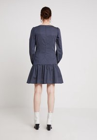 Vestido azul marino de lunares con mangas largas, corsé ajustado y falda acampanada. Presenta un dobladillo con volantes y botas blancas hasta el tobillo en contraste.