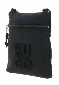 Sac bandoulière en nylon noir avec surface texturée, fermeture éclair et logo "HUGO" embossé sur le devant. Bandoulière ajustable incluse.
