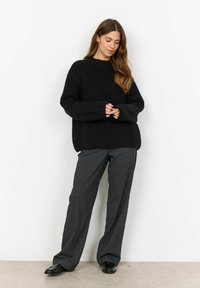 Maglione nero a costine con maniche lunghe, collo rotondo e vestibilità comoda, abbinato a pantaloni grigi su misura e scarpe nere.