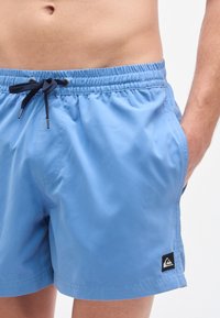 Μπλε μαγιό βερμούδα από ελαφρύ ύφασμα, με ελαστική μέση και κορδόνι, πλαϊνές τσέπες και μικρό λογότυπο.