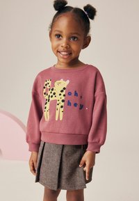 Sudadera rosa con un gráfico de leopardo y texto, combinada con una falda plisada gris. Presenta puños acanalados y un escote redondo.