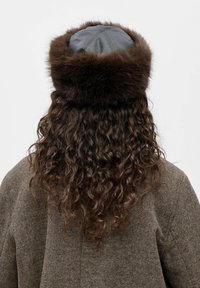 Chapeau en fourrure marron avec un dessus en cuir noir, présentant une texture lisse et une forme ronde, porté avec un manteau texturé marron.