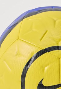 Kollane jalgpall, millel on tekstureeritud pind ja must logo ning aksendid. Näha on heksagonaalsed ja tähekujuline mustrid, millel on läikiv õmblus.